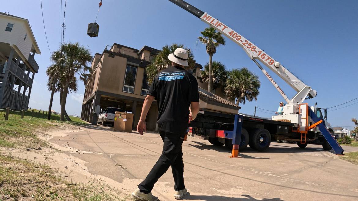 Coastal Comfort technician overseeing a crane lift of a new HVAC unit at a raised Galveston home